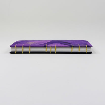 Spine of handmade book showing gold coptic stitching across purple and black boards