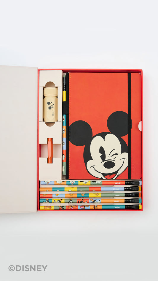 A Disney stationery gift set displayed in an open red box on a light gray background. The set includes a red notebook with a large Mickey Mouse face, several colorful pencils, a small beige bottle or container, and other stationery items.