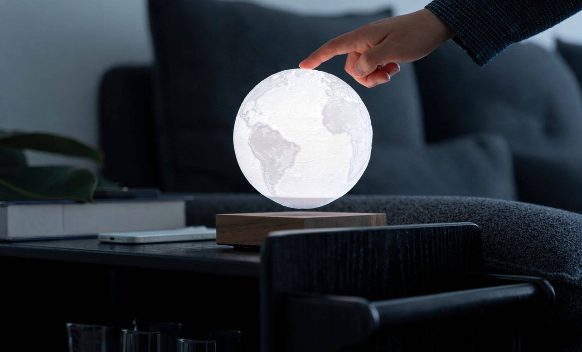 A hand steadying the unlit globe above its base in a dimly lit room