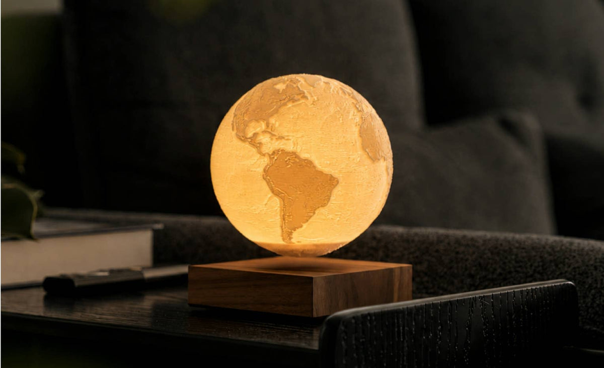 The Earth globe lit warm and floating above its base on a table in a dark room