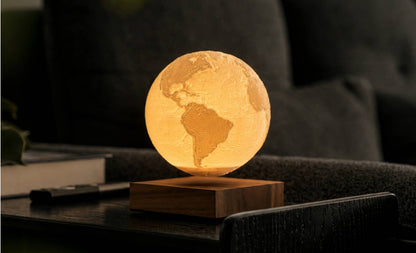The Earth globe lit warm and floating above its base on a table in a dark room