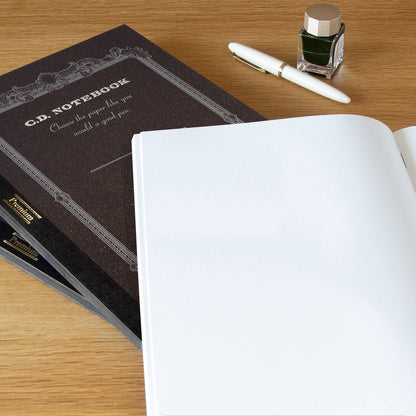Apica Premium A5 notebook open flat, blank pages, shown with a fountain pen and ink bottle on a wooden desk