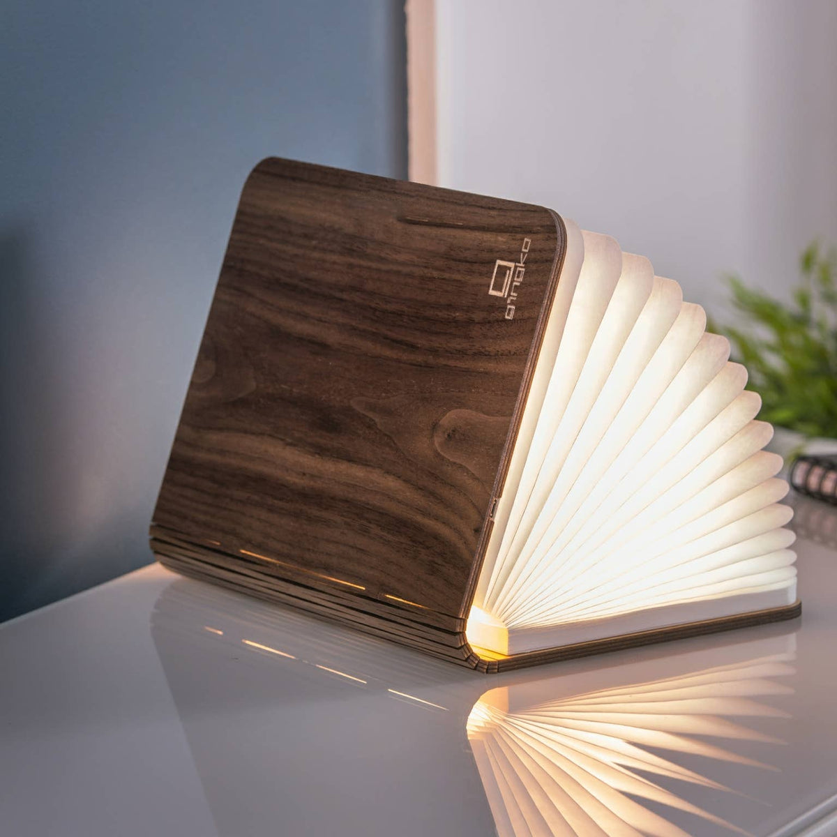 The walnut book light open on a table, its folded paper pages lit warm white